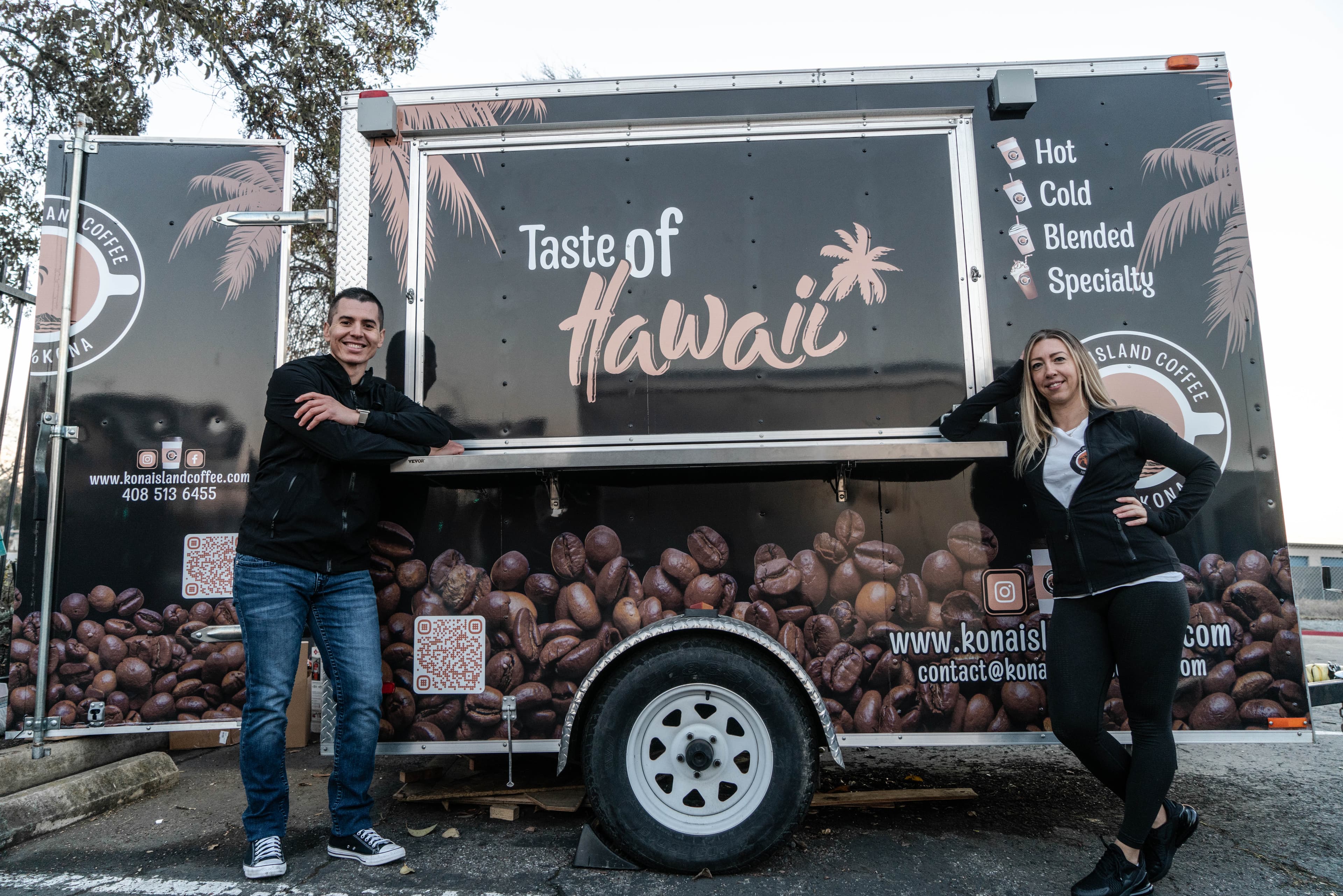 The Kona Island Coffee trailer, wrapped in coffee beans and palm motifs, with its service window open.